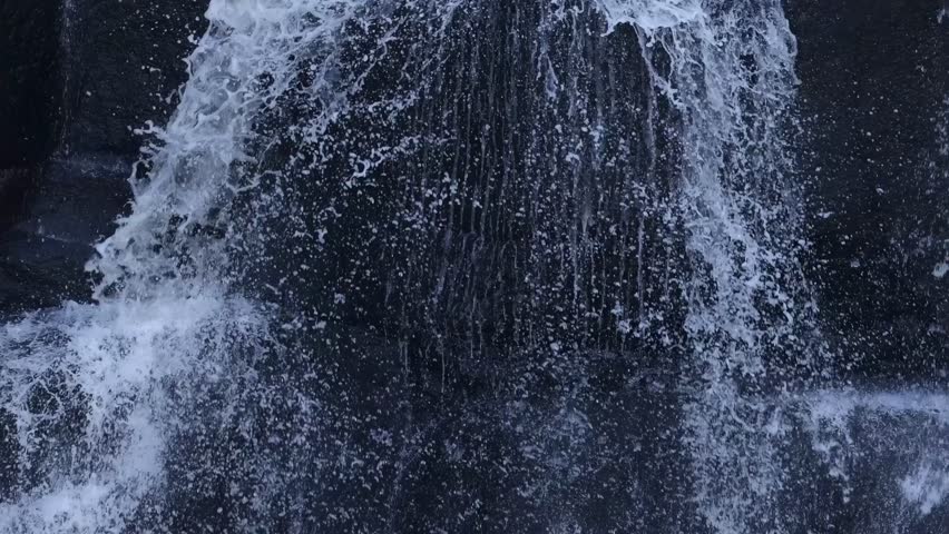 Detailed view of water splashing down a rocky surface, capturing the dynamic flow and texture.