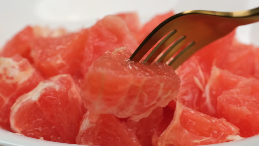 Eating juicy grapefruit. Take a slice of fresh red grapefruit with a fork