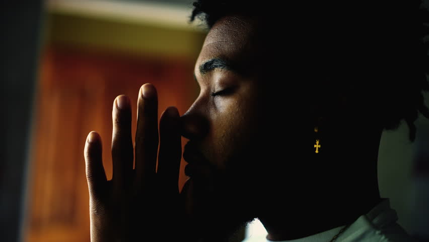 Profile close-up face of a young black man PRAYING to GOD. Meditative African American person with eyes closed engaged in devotion