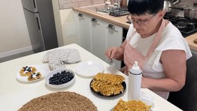 Elderly woman preparing a waffle breakfast with whipped cream and blueberries in a domestic kitchen - Powered by Shutterstock - Get 15% off with code: PIKWIZARD15