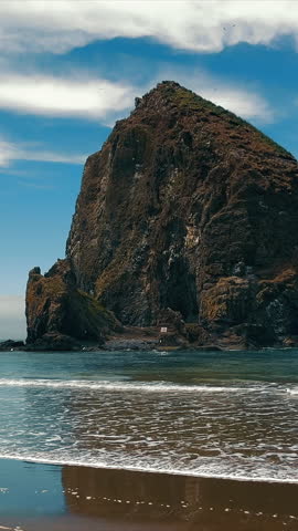 Giant rock formation on a calm beach. A massive rock formation rises from the ocean on a tranquil beach under a partly cloudy sky.