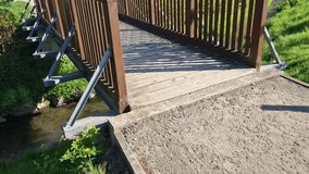 a park bridge with a wooden railing leads across the stream. The beams are fixed to a steel crossbeam that holds in a concrete foundation. road from gravel, in front of the bridge barrier - Powered by Shutterstock - Get 15% off with code: PIKWIZARD15
