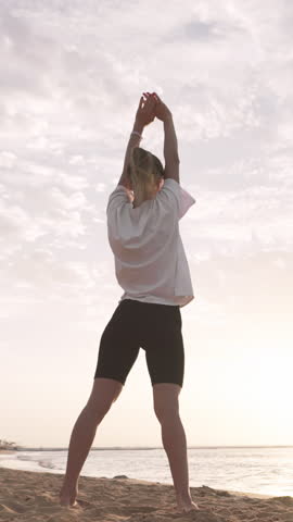 Active workout in morning on seashore, woman bending body, stretching muscles. Athletic lady training alone in sunrise or sunset, physical activity for stay healthy, yoga and fitness for stay slender
