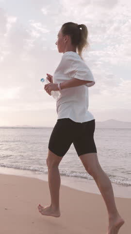 Beautiful slender woman running on picturesque shore of ocean, morning jog. Healthy lifestyle for stay young and slender in middle age, physical exercise outdoors, athletic female person training