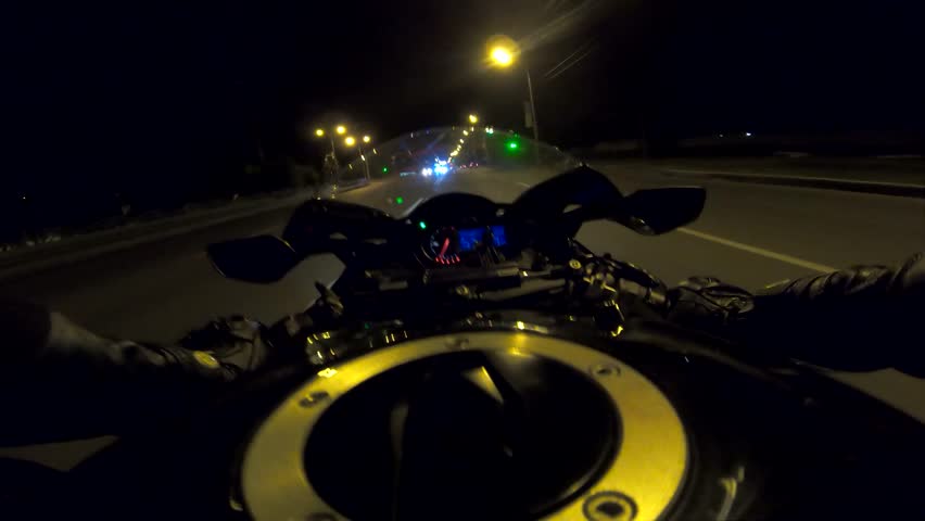 The viewpoint of motorcycle rider driving on motorbike at evening urban road on high speed. Male motorcyclist riding on modern sport bike in the illuminated city streets at night. Freedom concept. POV