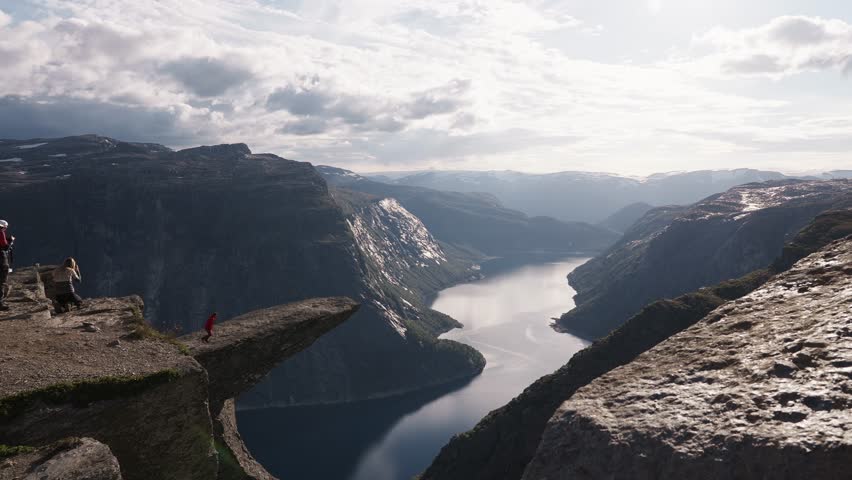 Hiker standing on Trolltunga rock ledge in Norway, overlooking fjord and mountains