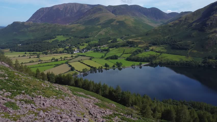 Smooth aerial video looking towards shores of Buttermere village and lake on beautiful summer's day - Lake District, UK