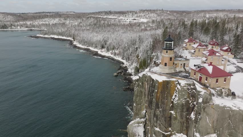 Split Rock Lighthouse And Houses On The Rocky Cliff With Snowy Forest In The Background In Minnesota, USA. - aerial shot