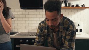 Multicultural couple in the kitchen during a quiet morning. He focuses on his laptop while she speaks on the phone. A salad in progress lies on the table as they share a calm routine. - Powered by Shutterstock - Get 15% off with code: PIKWIZARD15