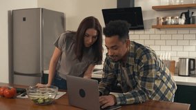 Multicultural couple in the kitchen during a typical morning. She finishes a phone call and looks over her partner's shoulder as he works on his laptop, sharing a calm, everyday moment. - Powered by Shutterstock - Get 15% off with code: PIKWIZARD15
