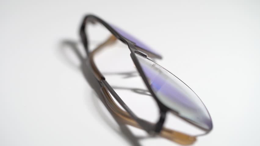 A pair of glasses with a blue lens sits on a white background. The glasses are tilted and appear to be broken. Scene is somewhat sad or melancholic