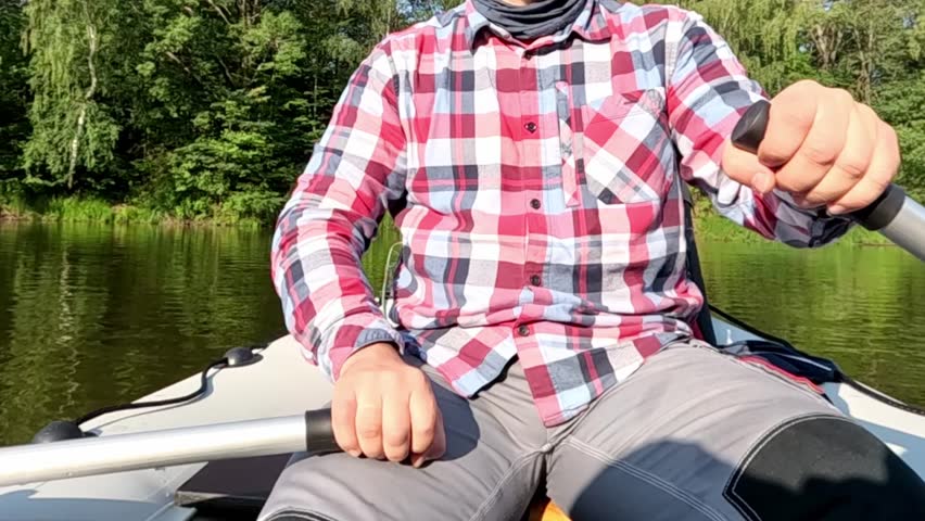 A man in a red and white plaid shirt is sitting in a canoe. He is holding a paddle and he is enjoying the activity