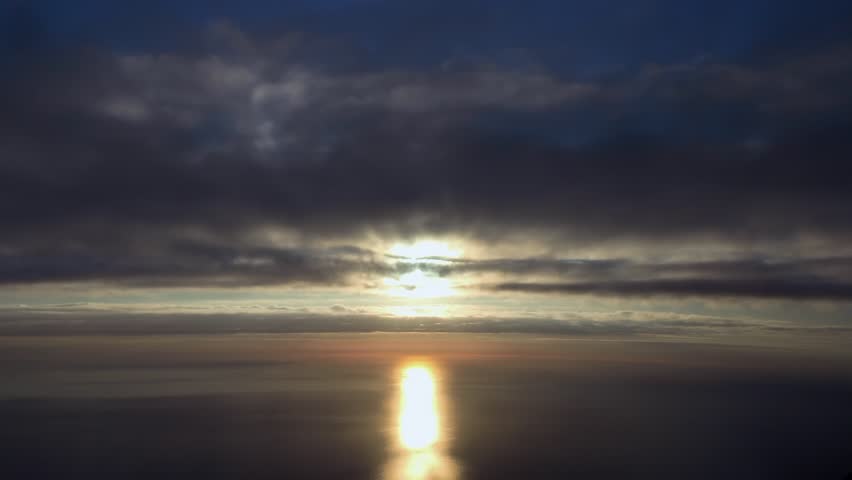 an immersive pilot POV taken from an airplane cockopit while flying under a dramatic clouded sky covered with darkening clouds with a radiant sun ahead over the ocean