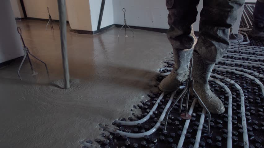 Workers are pouring concrete over underfloor heating pipes in a house under construction