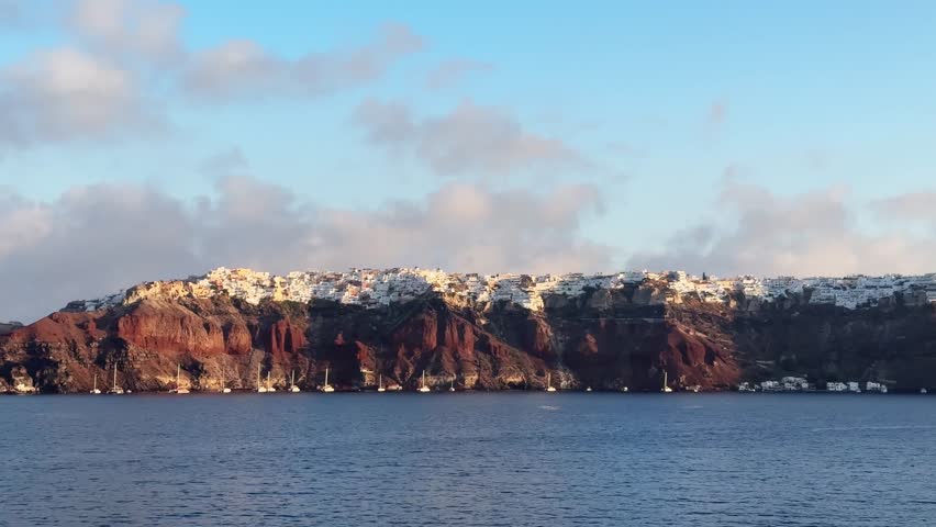 Santorini island, Greece. White architecture on the cliffs in Oia town. View from the sea at sunrise. Blue sea and the blue sky. Travel and summer vacation. 
