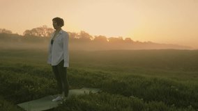 A girl in a white shirt doing squats at dawn in a misty field. The sky is orange and the grass is green - Powered by Shutterstock - Get 15% off with code: PIKWIZARD15