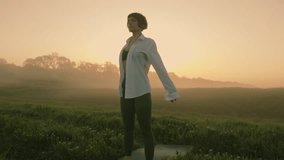 Handheld camera captures a young girl in a white shirt doing yoga at dawn in a field. The background is filled with fog. - Powered by Shutterstock - Get 15% off with code: PIKWIZARD15