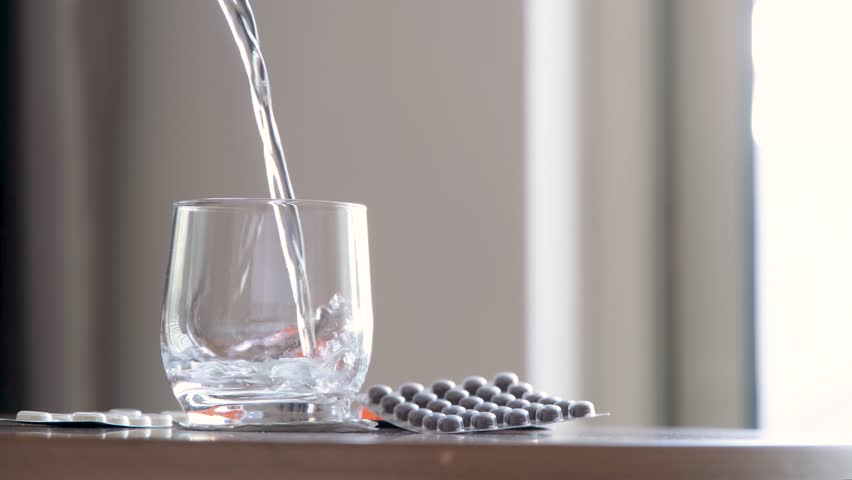 woman taking pills in the morning pouring water into glass sitting in the chair