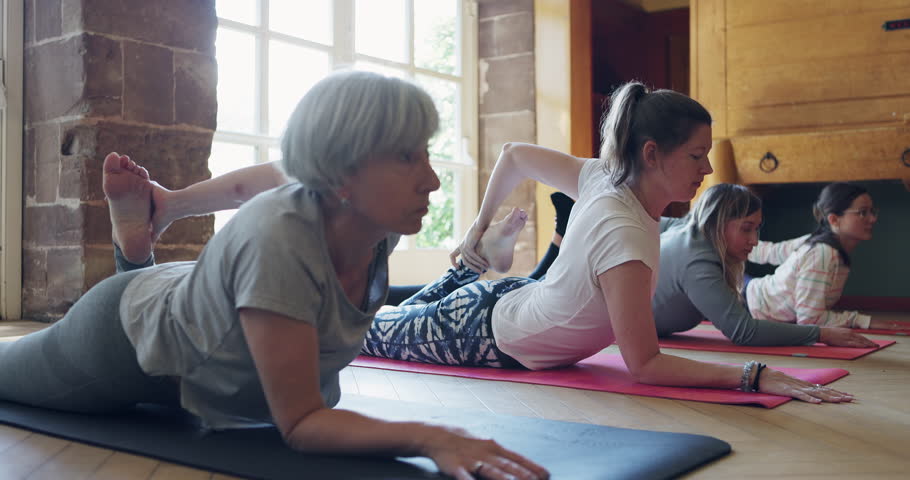 Yoga, stretching legs and people in class in pose for wellness, flexibility and mindfulness health. Fitness, personal trainer and group of women on gym mat for exercise, pilates training or mediation