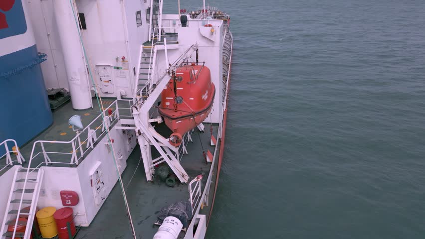Crew members conduct a lifeboat drill on the deck of a cargo ship. This training ensures safety procedures are practiced in case of emergencies while at sea.