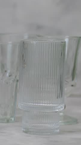 Glass Drinkware Collection with Gold Rim Detail on Gray Surface, Panning Shot, Vertical Video