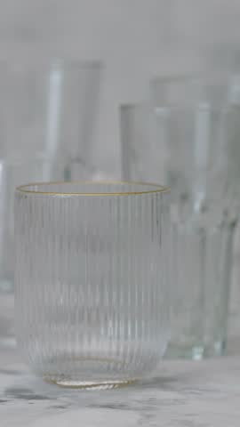 Glass Drinkware Collection with Gold Rim Detail on Gray Surface, Panning Shot, Vertical Video