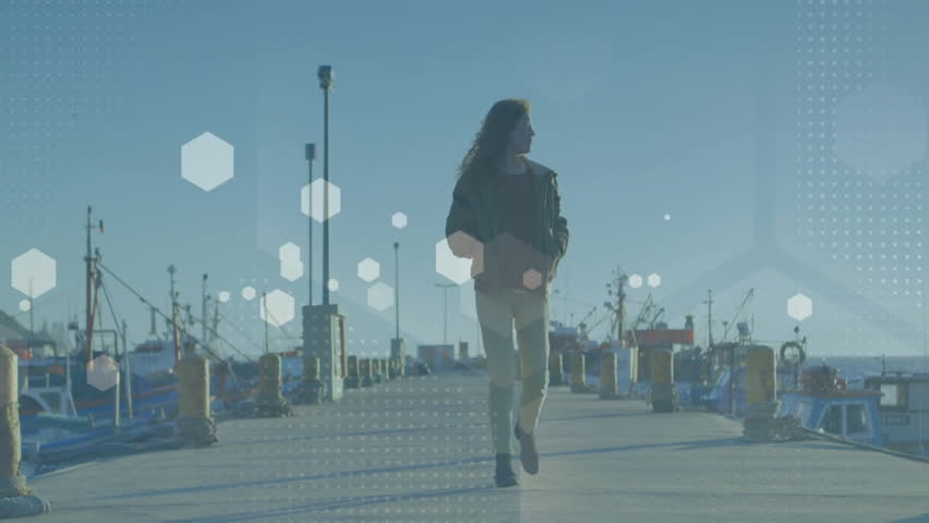 Woman walking down concrete harbor pier, showing technology hexagonal data overlays on bollards. Harbor, waterfront, nautical, voyage, maritime, coastal, leisure