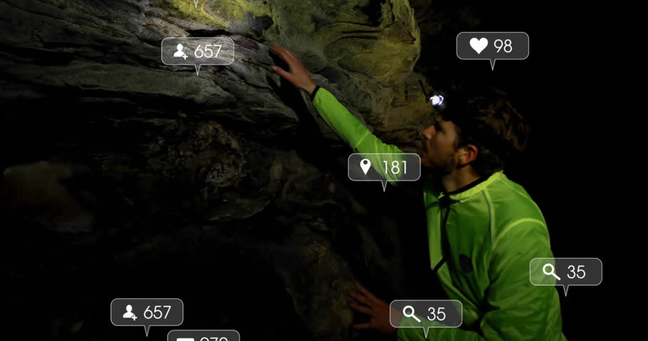 Male spelunker with headlamp examining cave wall showing floating social media icons for technology. Adventure, exploration, rugged, nighttime, digital, connectivity, discovery