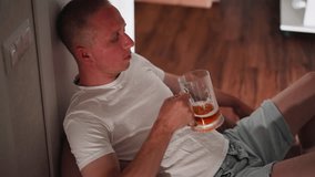 Man sitting casually on floor against wall drinking beer from transparent glass mug wearing white t shirt and light shorts in cozy indoor setting with wooden floor - Powered by Shutterstock - Get 15% off with code: PIKWIZARD15