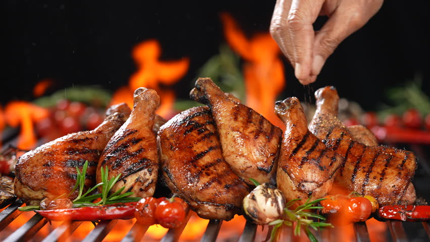 Chicken thighs grilled on hot barbecue charcoal flaming grill with spices sprinkled on top. Juicy chicken meat roasted on bbq grill.