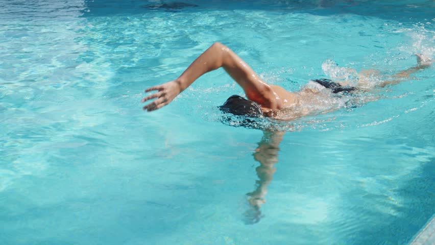 Professional swimmer swims in an outdoor pool. Young man swimming in pool in freestyle style - Slow motion video. Young pro swimmer athlete conducts a training session. Healthy lifestyle  concept.