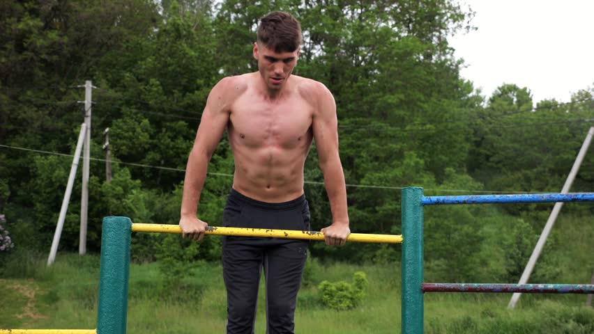 Hardy shirtless sportsman doing push ups on horizontal bar at nature. Strong and muscular guy training at sports ground. Young athletic guy exercising outdoor. Concept of active and healthy lifestyle