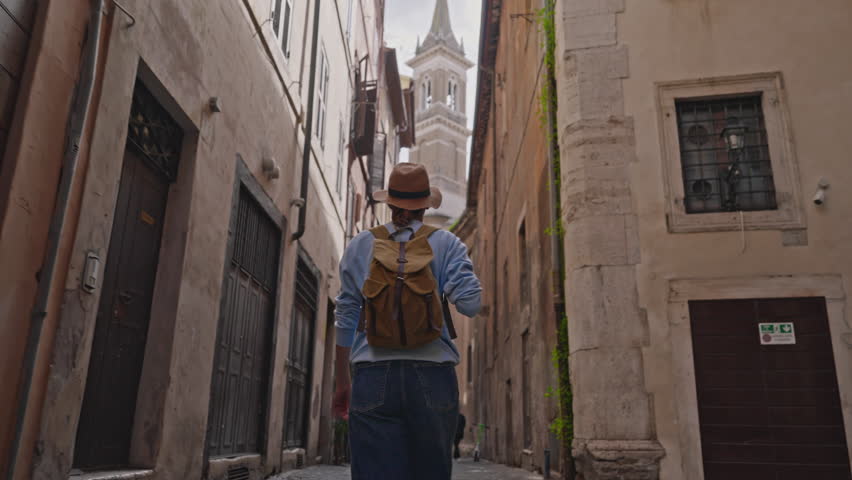 Woman tourist in hat with backpack walking down old street in Rome, Italy. Girl looking around in Rome old city