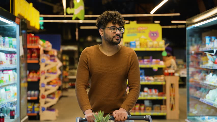 Arab man with shopping cart walking through supermarket aisle