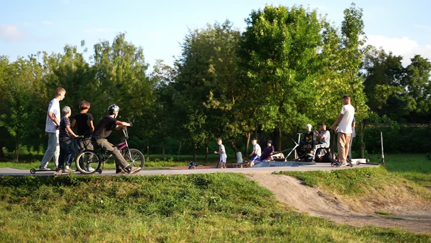 Rivne, Ukraine - June 2, 2024: FGroup of kids with bikes and scooters at a skatepark, Outdoor gathering of children riding BMX bikes and scooters at sunset