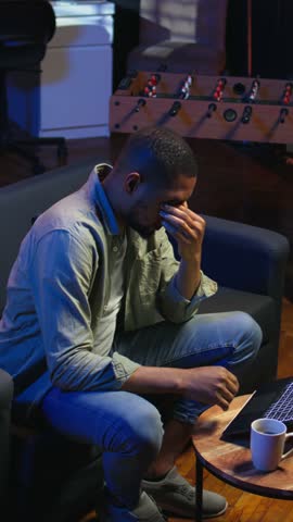 Vertical Video African american person receiving some bad news while doing remote work tasks, feeling overworked and under pressure to complete all his assignments. Young adult deals with burnout