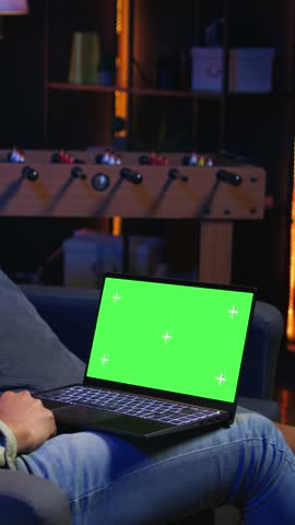 Vertical Video African american remote worker uses chroma key screen on gadget to work in the living room, sitting on the couch in his modern stylish living room. Happy young adult on the internet