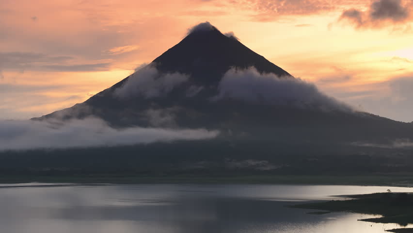 Experience the breathtaking aerial view of a stunning sunrise over Arenal Volcano, shrouded in mist and surrounded by lush forests near Laguna de Arenal in beautiful Costa Rica, rich in biodiversity