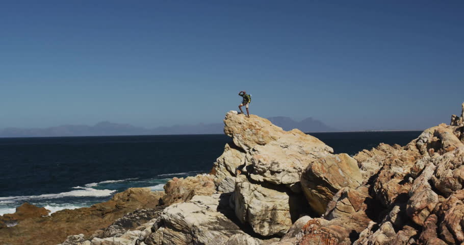 Man hiking on rocky coastline, surveying ocean with floating technology HUD graphs and data grids. Adventure, exploration, rugged, technology, futuristic, outdoor, landscape
