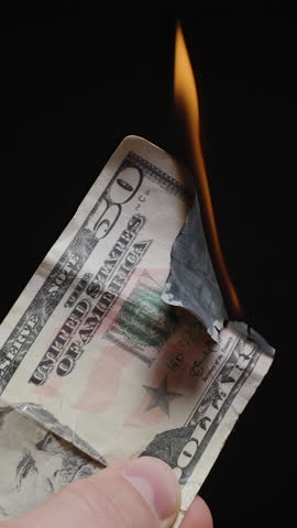 Vertical video. Burning Fifty Dollar Bill Held by Fingers with Upper Edge Blackened by Flame against Black Background, Mid Burn Stage in Close Up, Concept of Economic Crisis