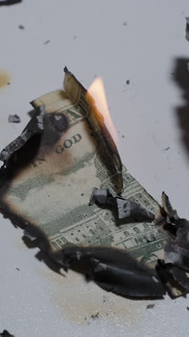 Vertical video. Burnt and Partially Burning Pieces of a Fifty Dollar Bill Scattered on White Table Surface with Ash and Flame Visible, Overhead View, Concept of Financial Destruction