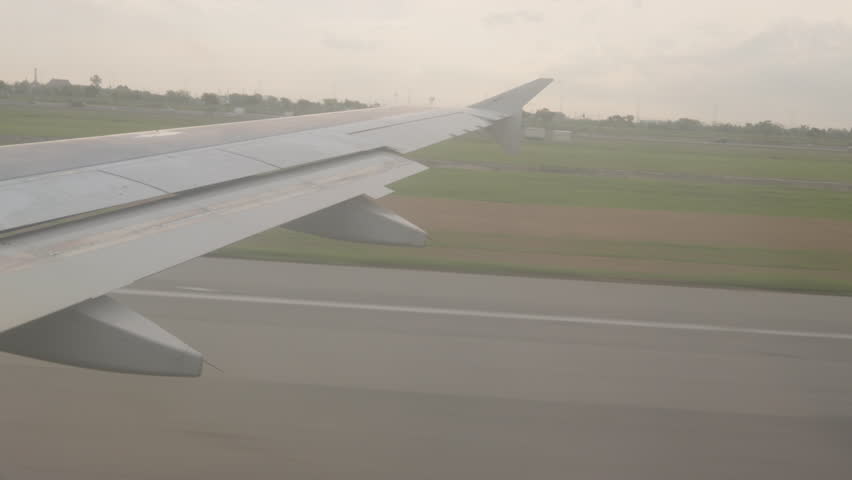 View from Window as Airplane Accelerates on Runway During Takeoff with Wing Visible and Ground Motion Blur Under Soft Light, Early Flight Phase Concept