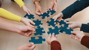 A diverse group of hands collaborates to connect colorful puzzle pieces on a wooden table. This image captures teamwork, creativity, and effective problem-solving in a professional setting. SACTR - Powered by Shutterstock - Get 15% off with code: PIKWIZARD15