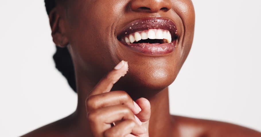 Happy woman, skincare and sugar scrub on lips for beauty treatment, laugh or natural exfoliation. Closeup, mouth or model apply cosmetics on face for glow, peeling or clean on white studio background
