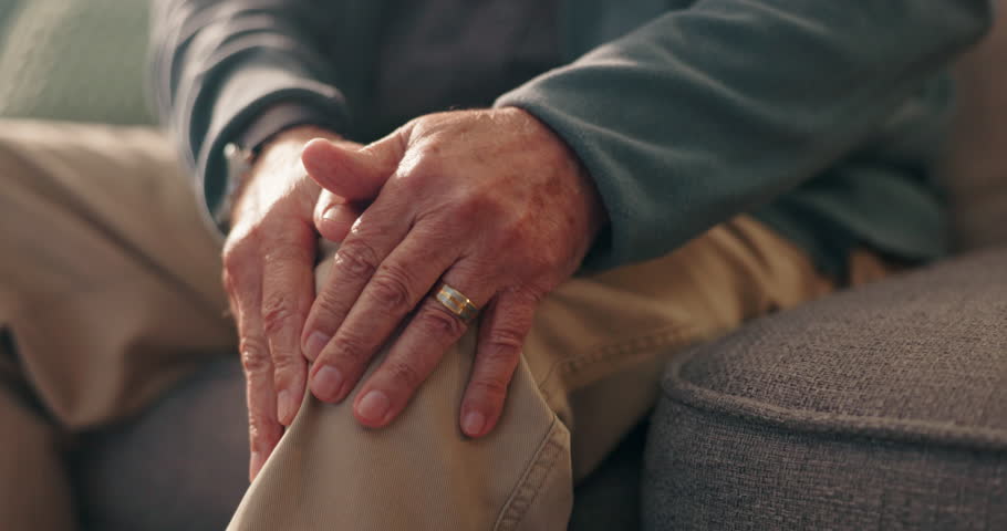 Hands, knee pain and old person with injury, arthritis or osteoporosis with muscle or joint ache in home. Torn ligament, discomfort and bone fracture, man on sofa with leg pressure or tension massage