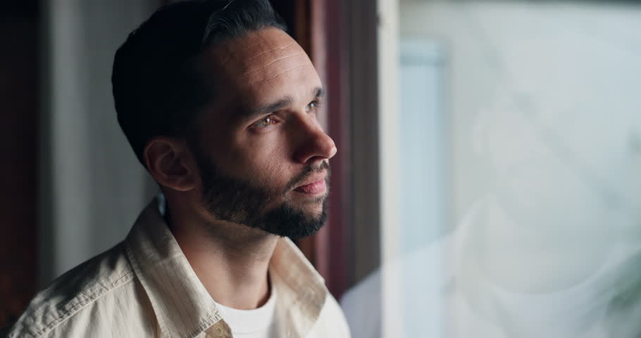 Sad, thinking and window with man at home for mental health, memory and psychology. Mistake, fear and loneliness with male person in living room of house for depression, grief and reflection