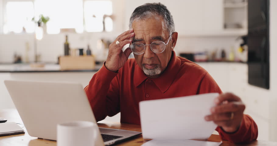 Senior man, laptop and documents in financial crisis for debt, mortgage or tax in kitchen at home. Elderly, male person or pensioner with computer or paperwork for finance, bills or expenses at house