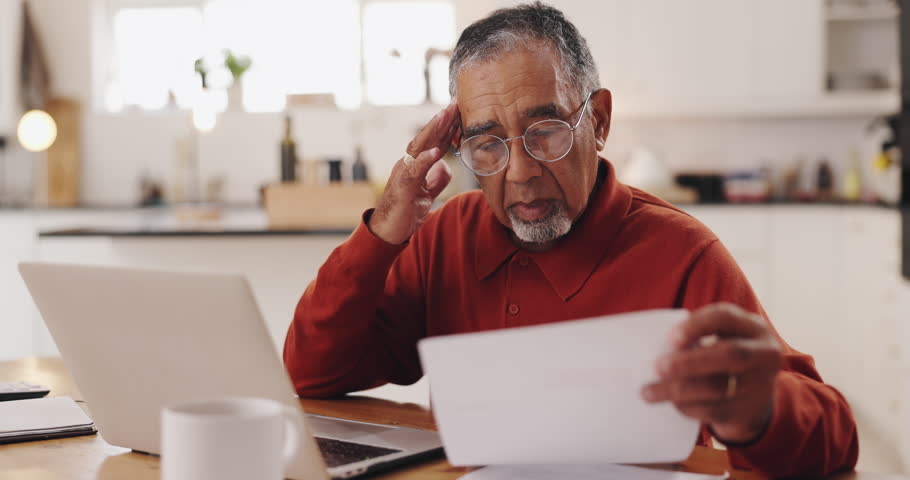 Senior man, laptop and documents in financial crisis for debt, mortgage or tax in kitchen at home. Elderly, male person or pensioner with computer or paperwork for finance, bills or expenses at house