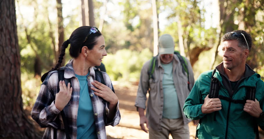 Hiking, adventure and mature group in woods, walking and journey for backpacking, outdoor and environment. Trekking, talk and traveller on holiday in nature, forest and people on trip for exploration