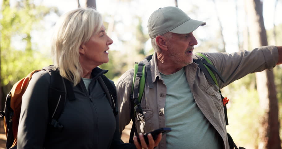 Phone, hiking and couple in forest for direction, destination discussion or lost in woods. Mobile, senior man and woman trekking, reading map or pointing for navigation app with location for travel
